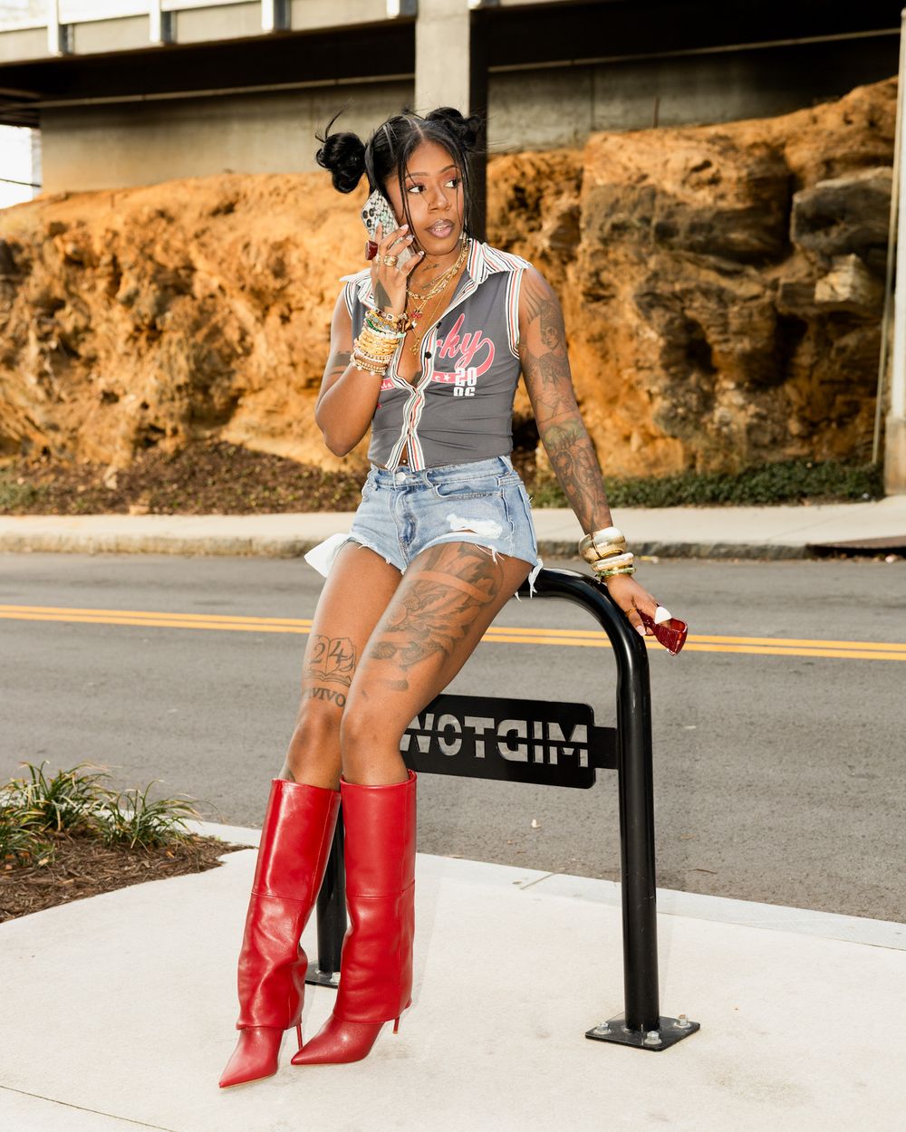 Woman sitting on a bench wearing red boots and denim shorts in an outdoor setting with rocky background.
