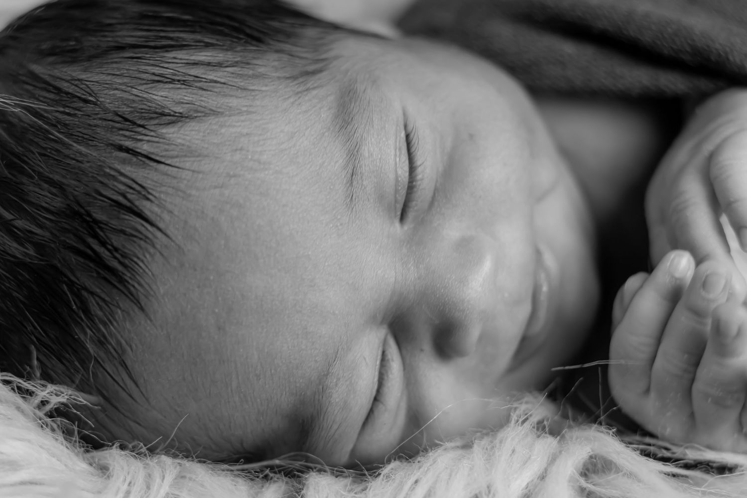 Close-up black and white photo of a sleeping baby with dark hair.