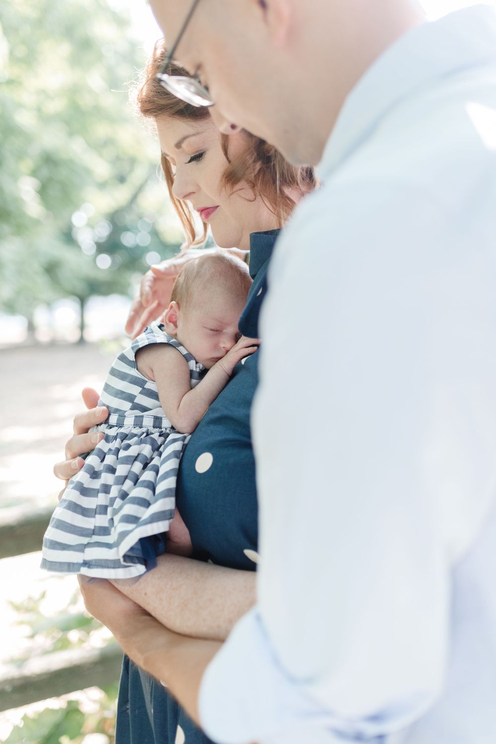 Mother holding newborn baby girl next to dad during golden hour outdoor Toronto family photoshoot in High Park - natural family photography.