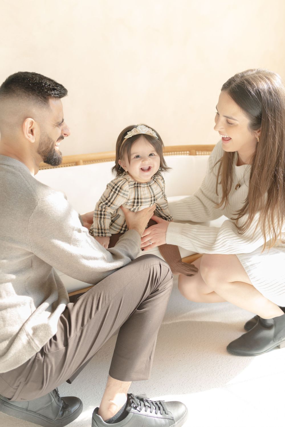 Family photography in Toronto - baby girl smiling while sitting on couch while smiling parents admire her at Mint Room Studios