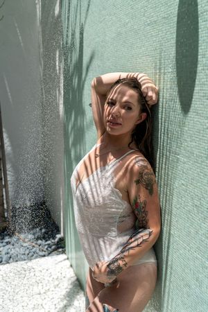 Person in white top poses against turquoise wall with dramatic shadows and natural lighting creating artistic effect.