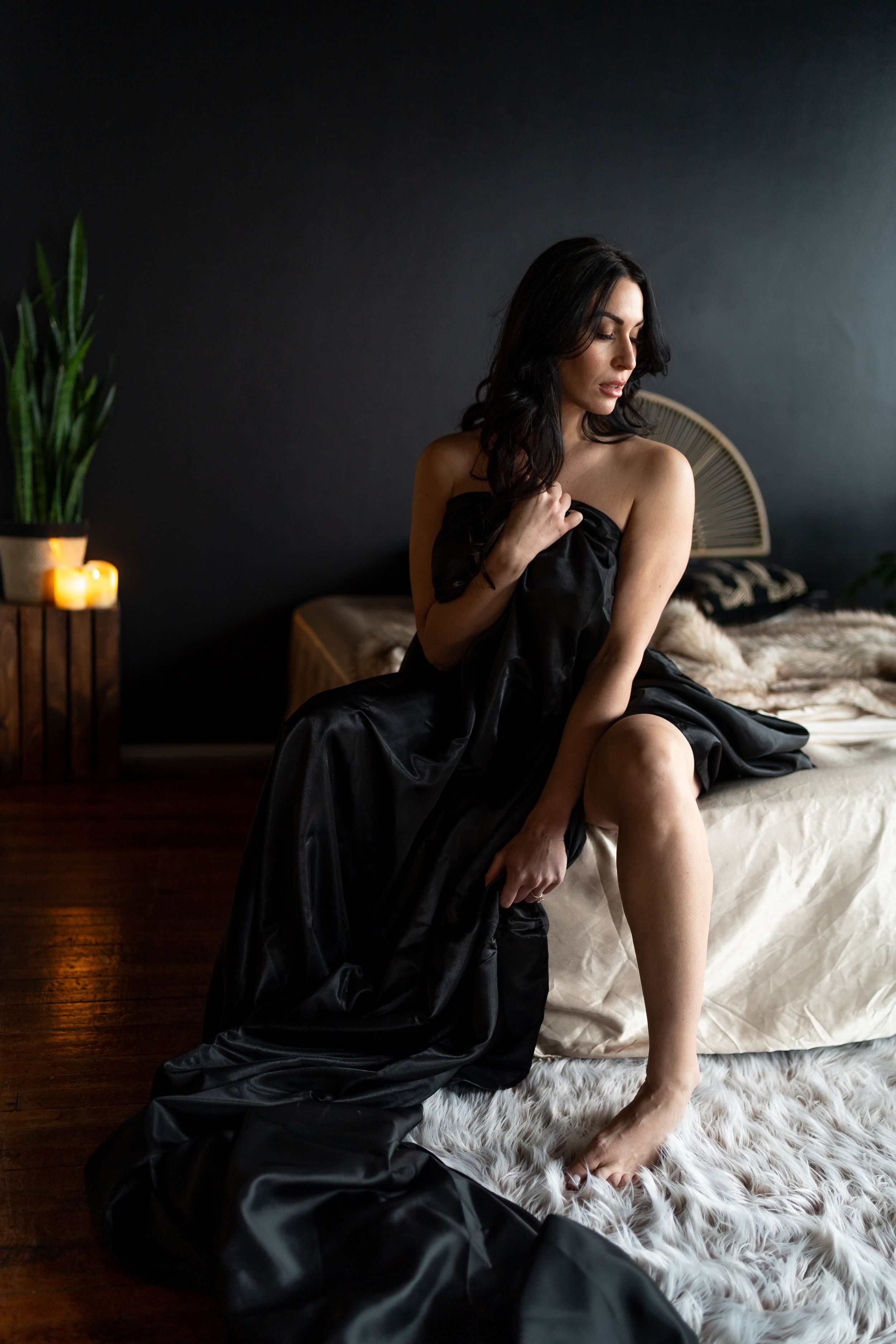 Moody boudoir photography series showing figure in black dress on white bedding with dramatic lighting and dark background.