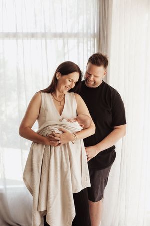 A couple in black and beige outfits share tender moments in three connected photos by a bright window.