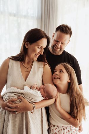 A family of four shares tender moments together in a series of intimate black and white portraits by a window.