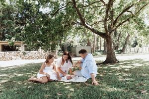A family enjoys a sunny afternoon picnic together under shady trees in a peaceful park setting.