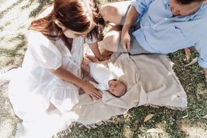 A couple sits together on grass in matching white outfits during an intimate outdoor photoshoot.