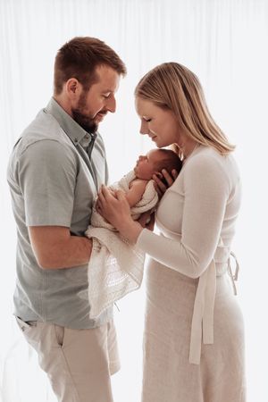 A couple shares tender moments with their newborn baby in a bright white studio setting during a family photoshoot.