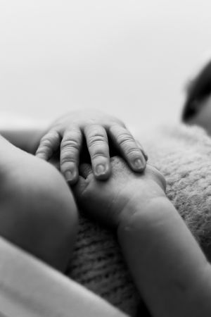 Close-up black and white photograph of tiny baby fingers grasping gently on soft fabric.