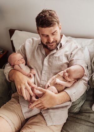 A tender moment between parent and infant resting together on a cozy gray couch in soft natural lighting.