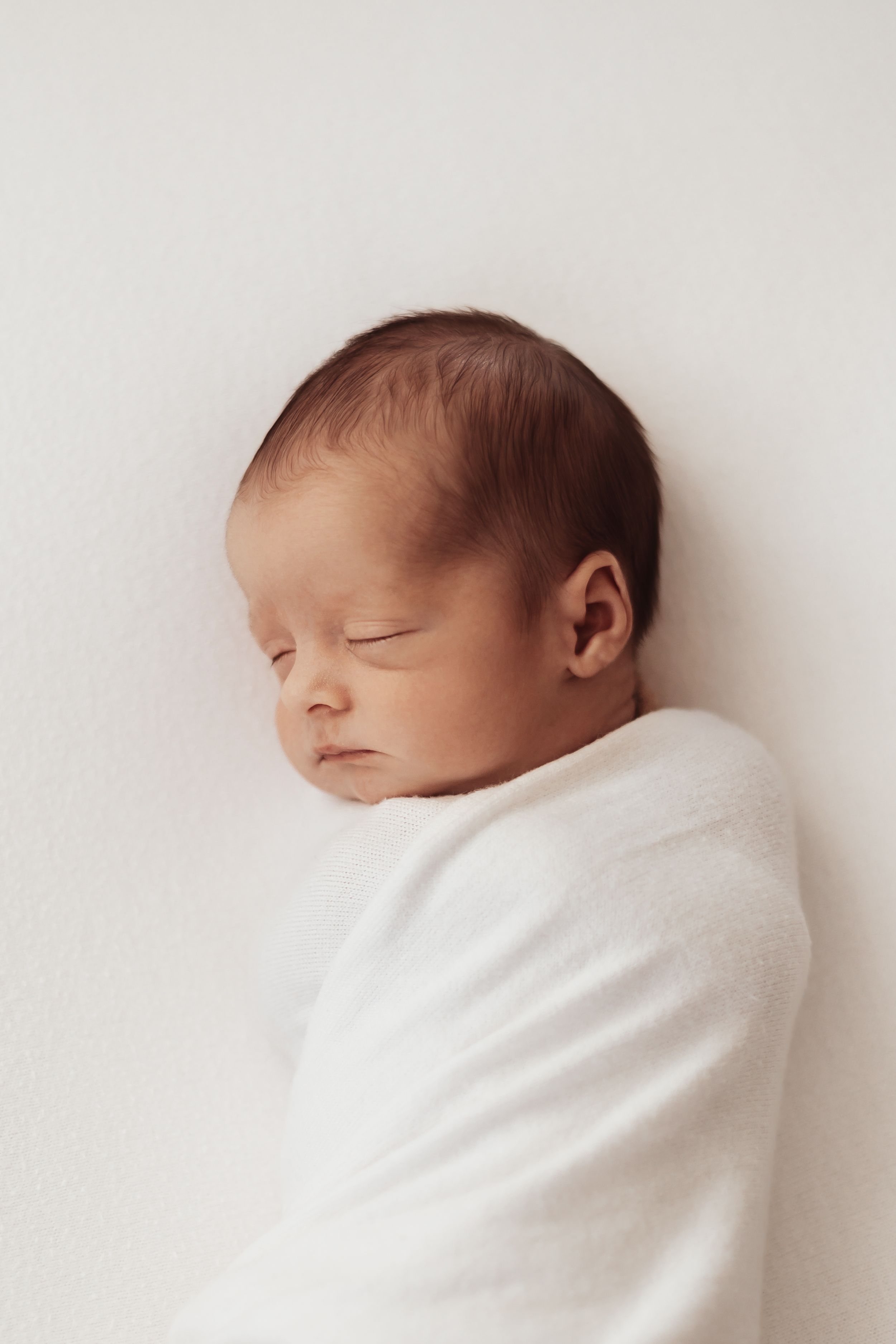 A sleeping newborn baby swaddled in white blankets against a light background.