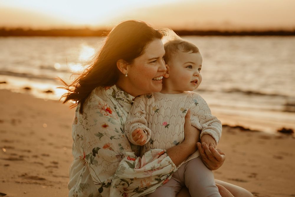 Mother and toddler sharing a joyful moment on a sandy beach at golden sunset hour.
