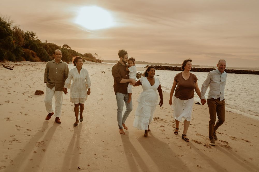 A group of people walking along a misty beach shore at sunset in a continuous sequence of photos.