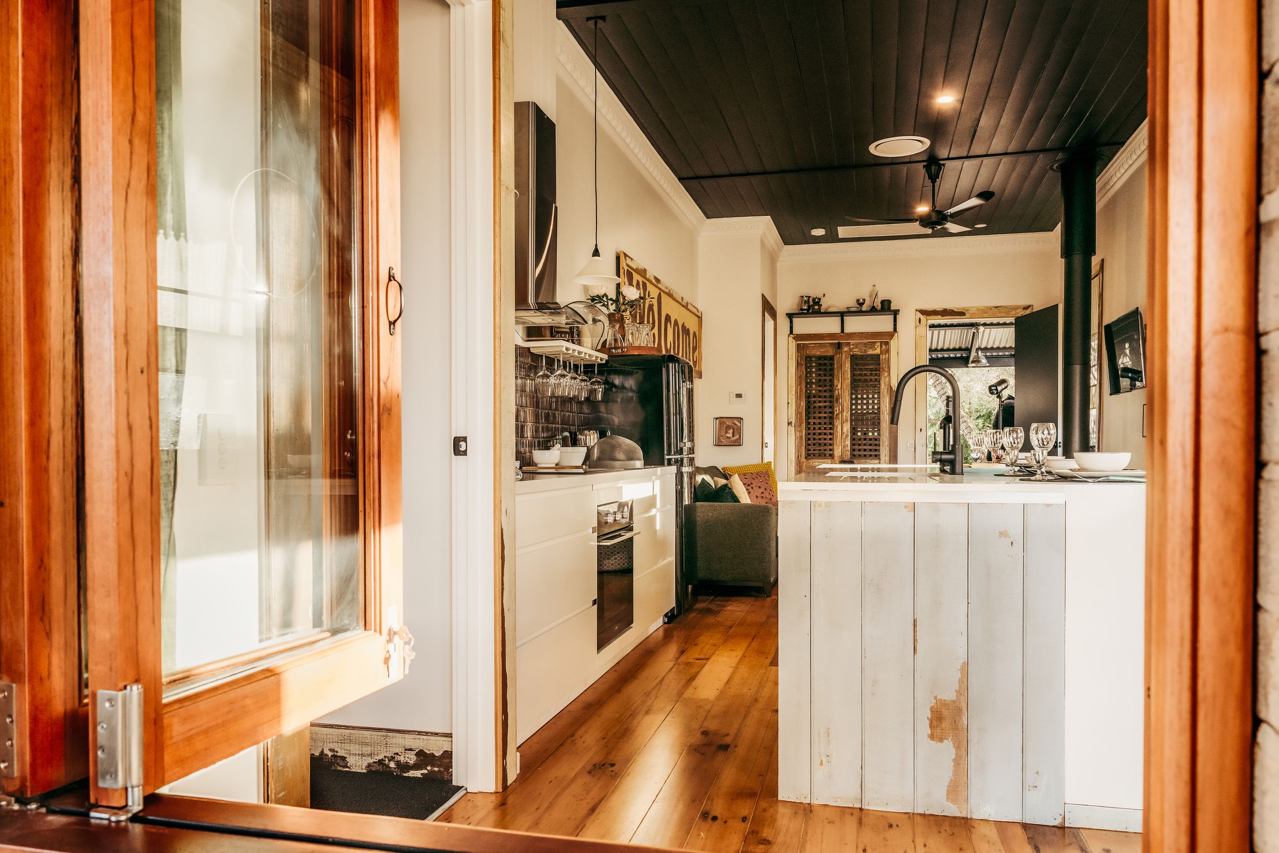 Cozy rustic kitchen interior with wooden floors, white cabinetry, and warm natural lighting through glass windows.