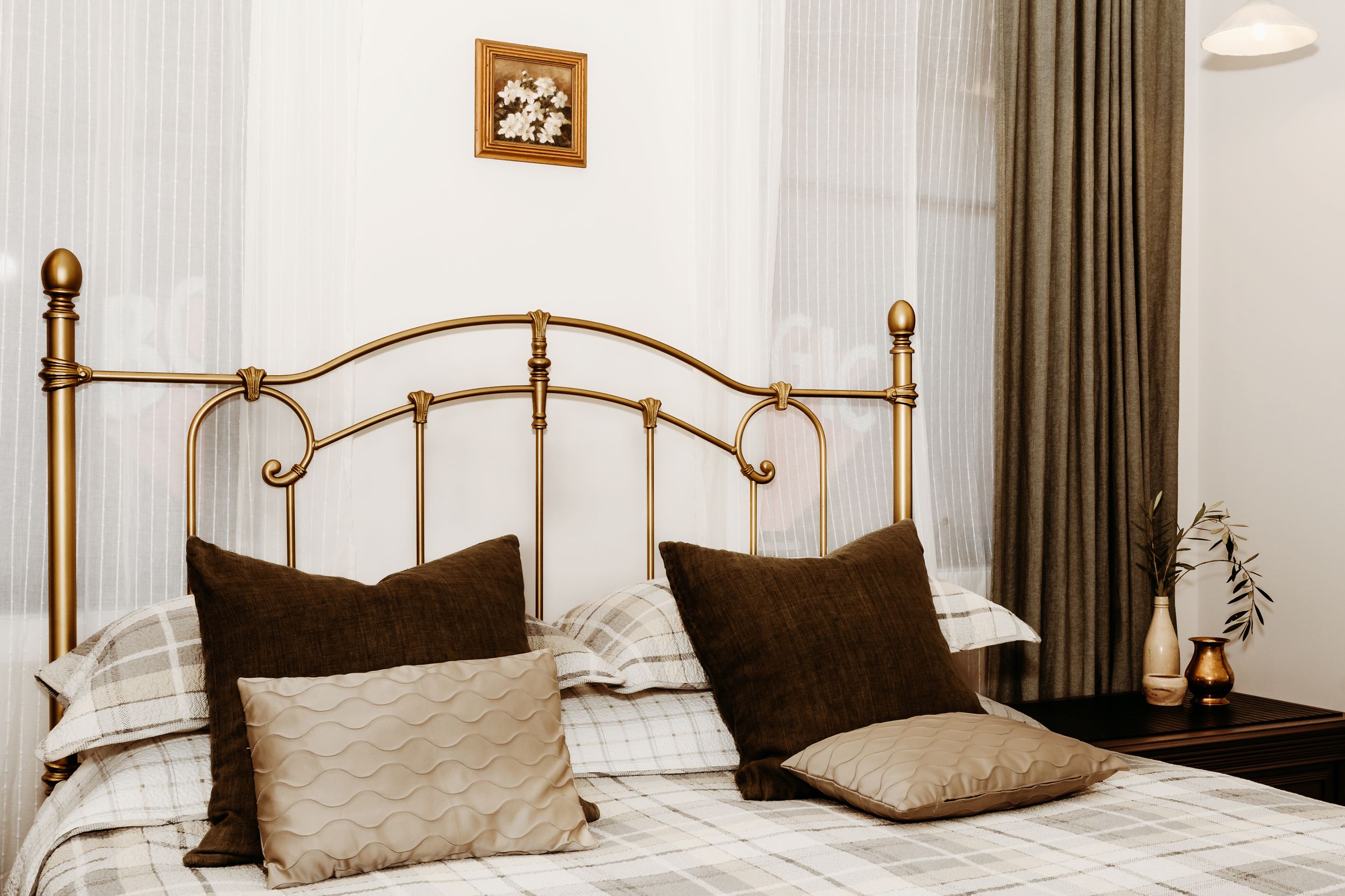 Elegant brass bed frame with neutral beige and brown pillows against white walls in a cozy bedroom setting.