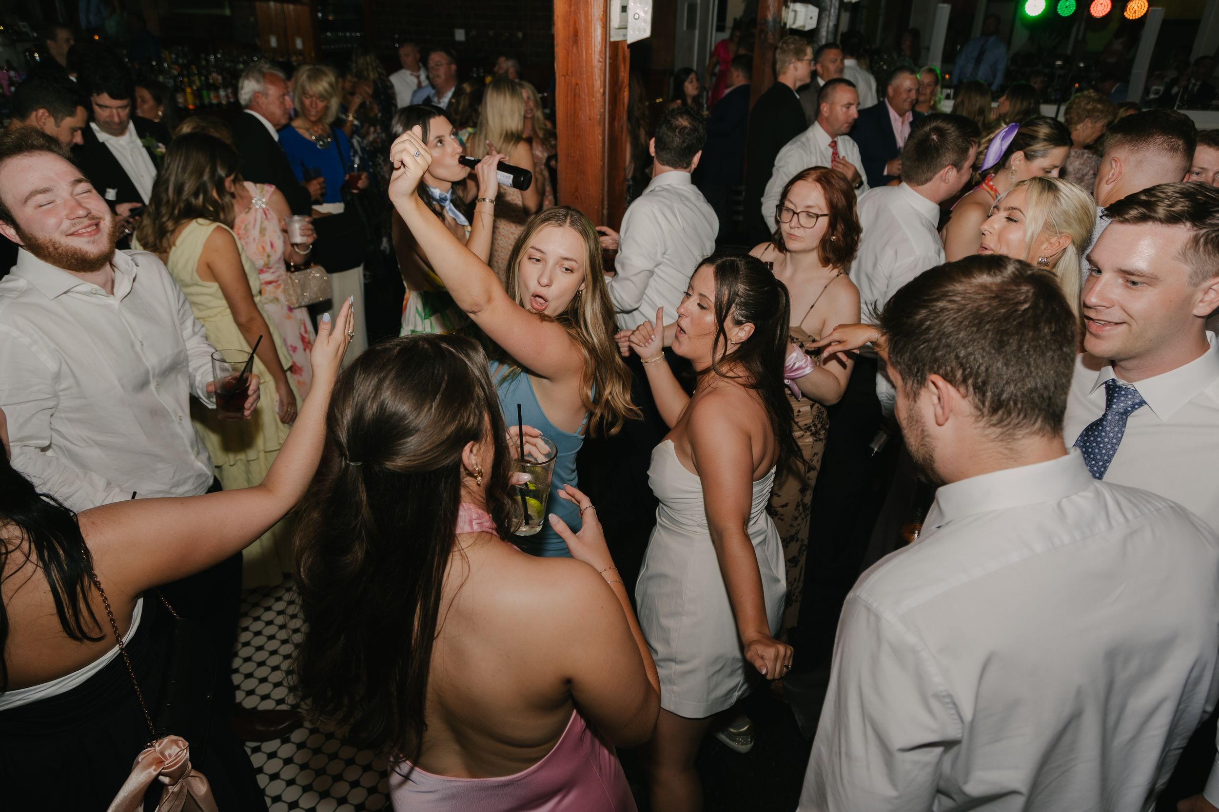 Wedding reception scene with guests in coral and burgundy dresses on a dance floor.
