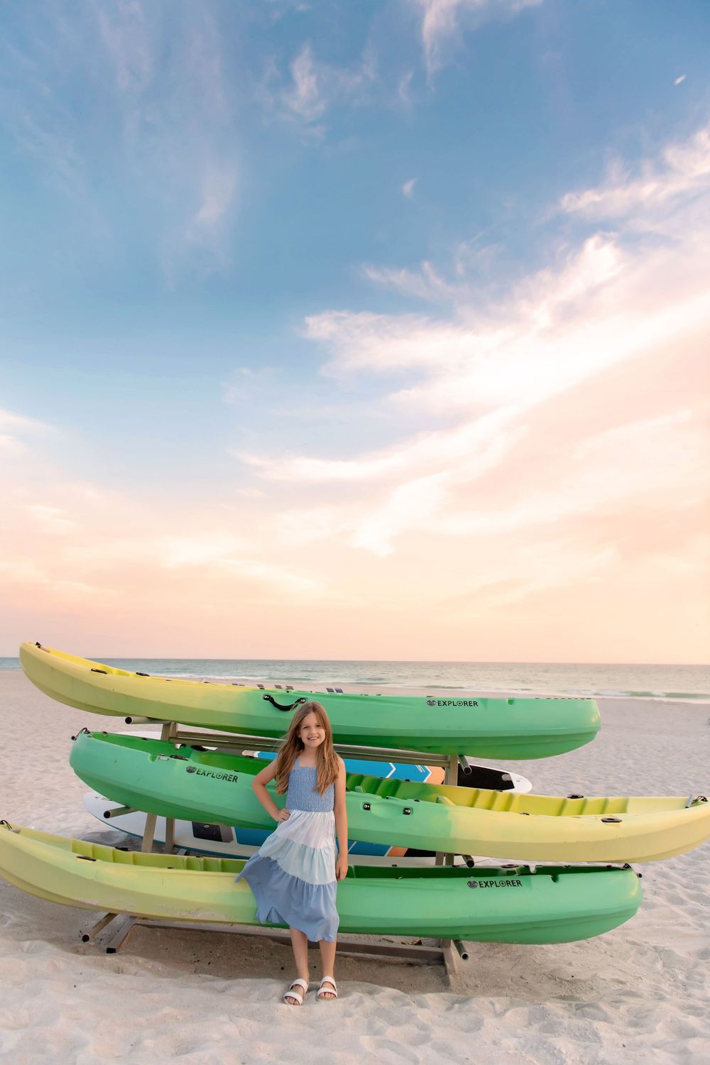 Colorful kayaks lined up on white sand beach during sunset with blue skies.