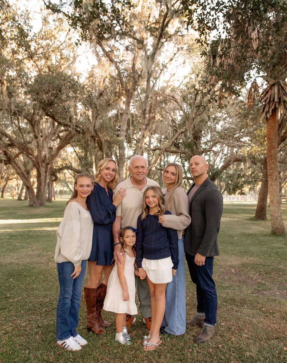 Extended family group poses together for a portrait under Spanish moss trees in a park setting.