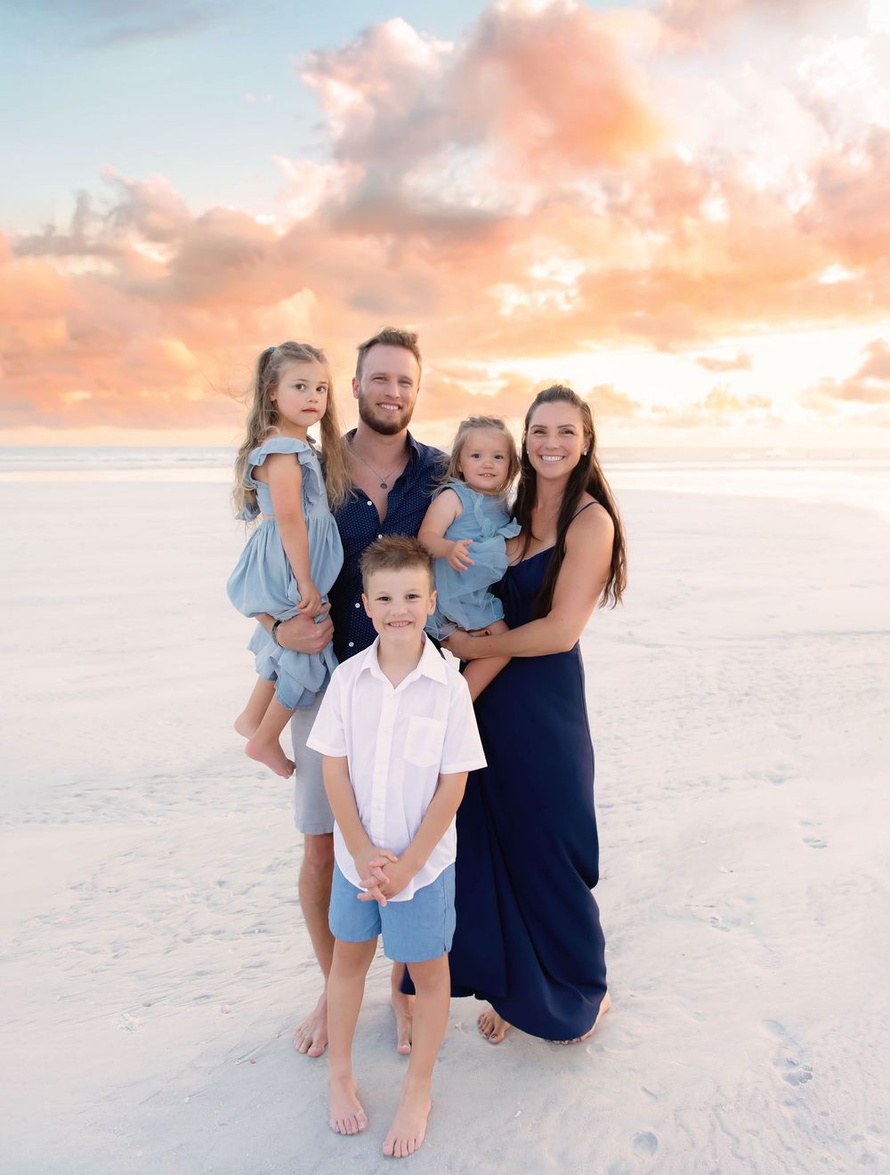 Beach family portrait session with coordinating blue and white outfits at sunset.
