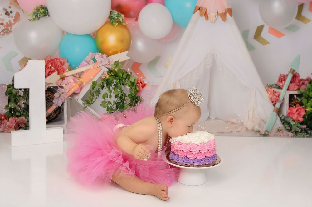 A festive birthday setup with pink tulle, balloons, and a colorful cake against a floral backdrop.
