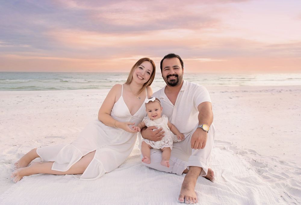 Family enjoying a sunset photoshoot on a white sandy beach with soft pastel skies in the background.
