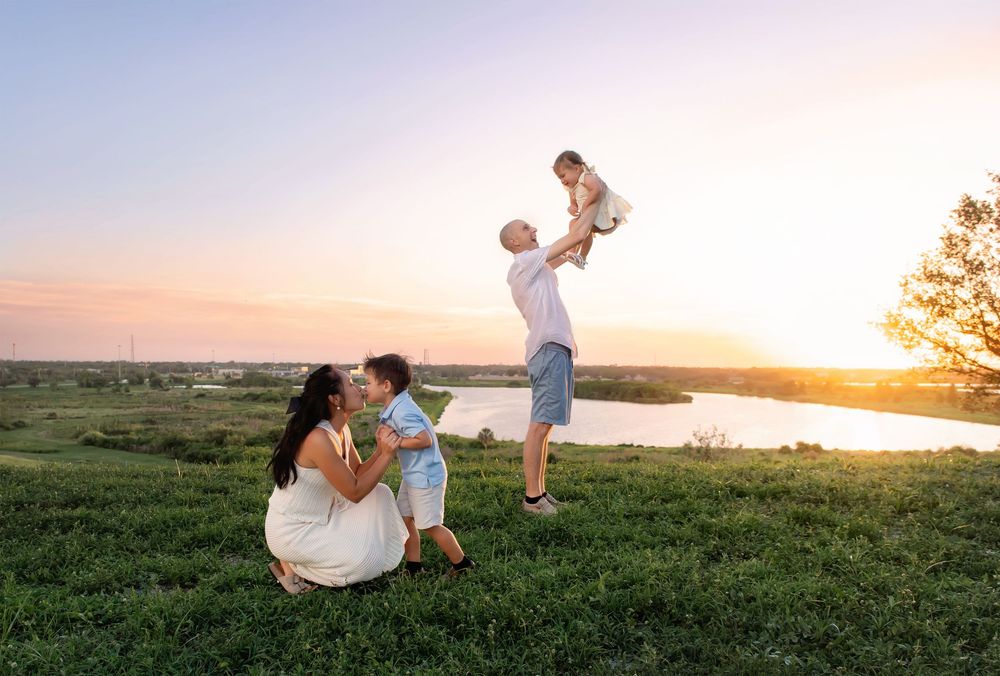 Playful family photos at sunset in grassy field by the water.