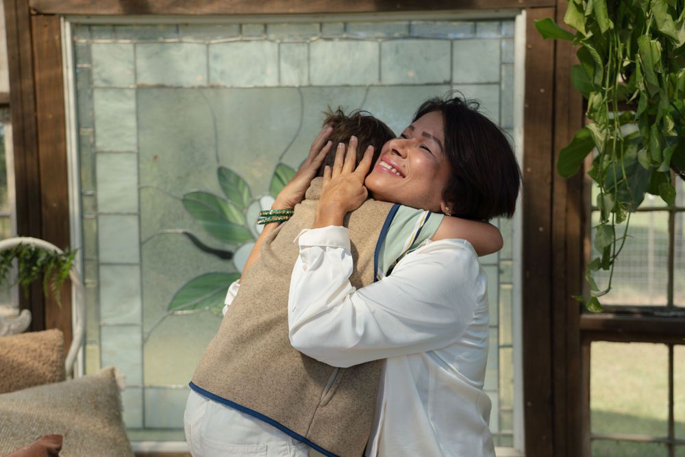 Family members share joyful embraces and laughter in an outdoor setting with white columns and greenery.