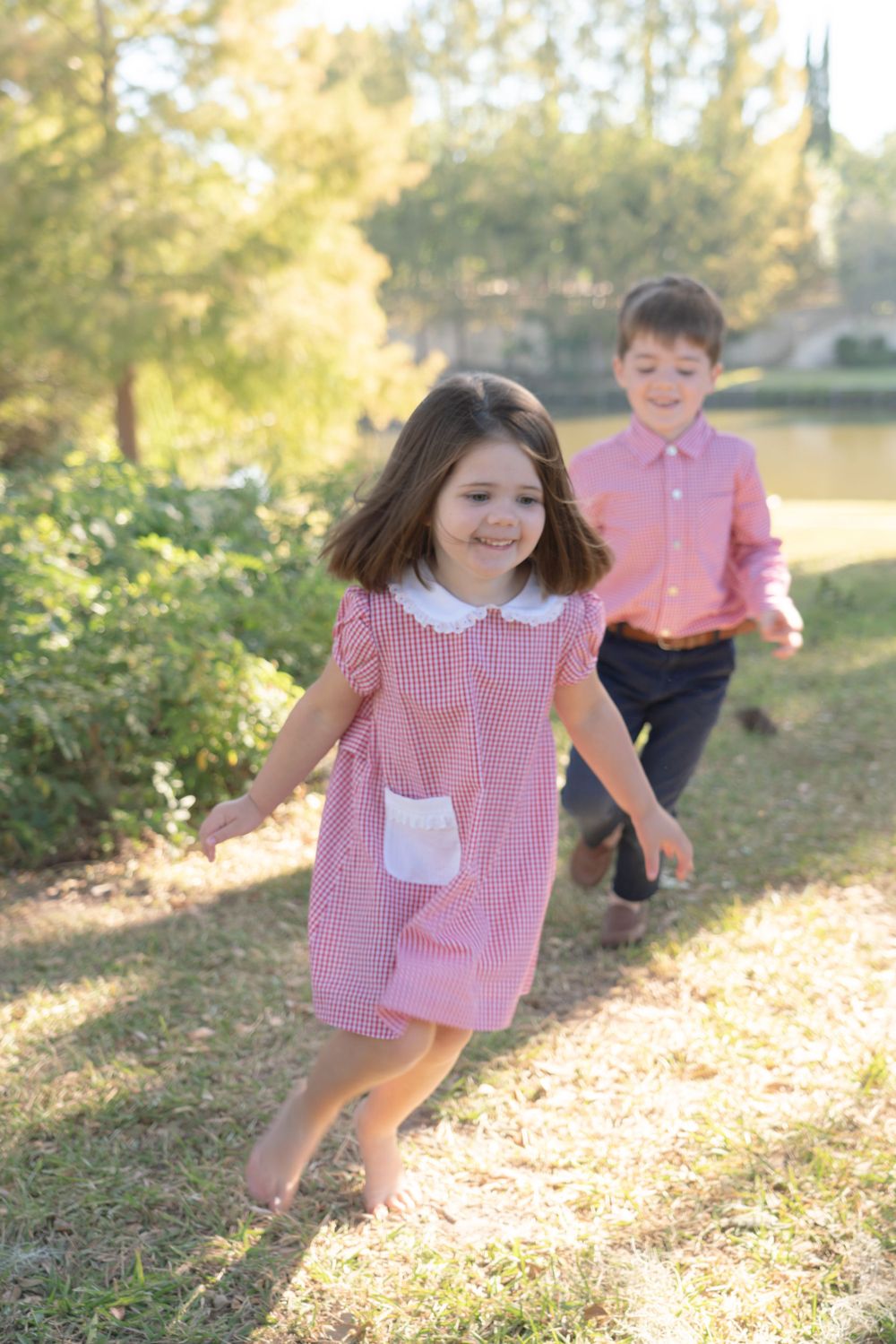 Playful children in red gingham outfits running and playing in a sunlit outdoor setting.