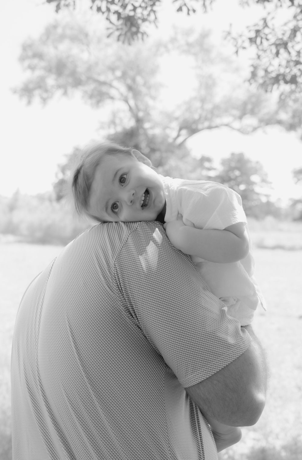 Black and white portrait of baby being held up against soft natural background.