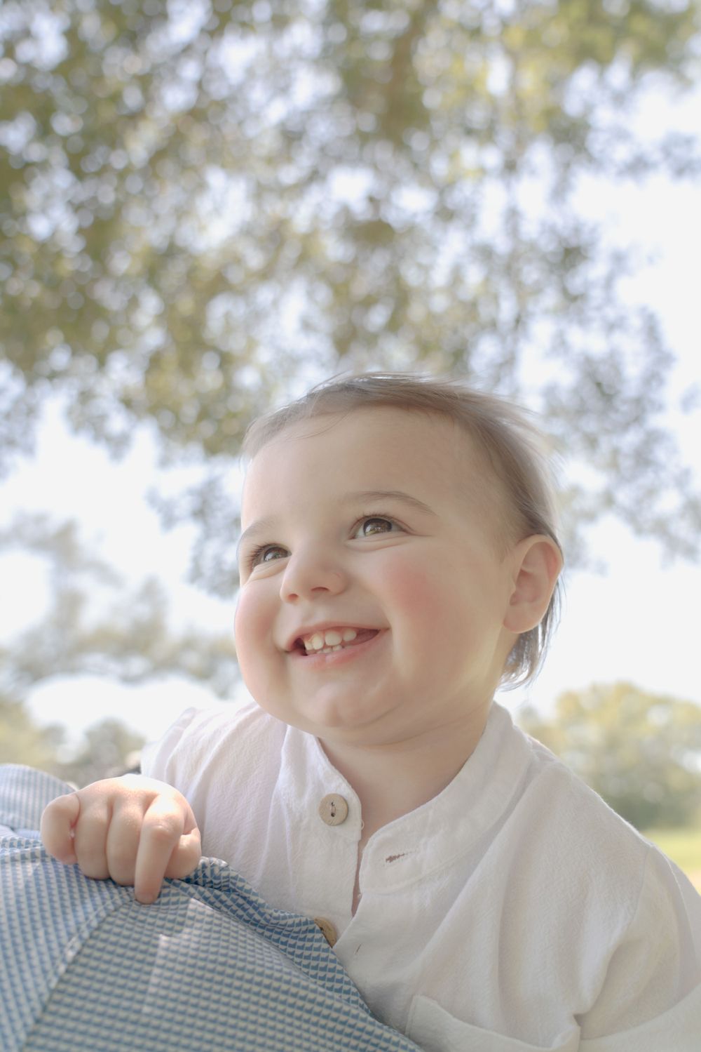 Close-up portrait of a smiling baby wearing a white collared shirt against a soft blurred background.