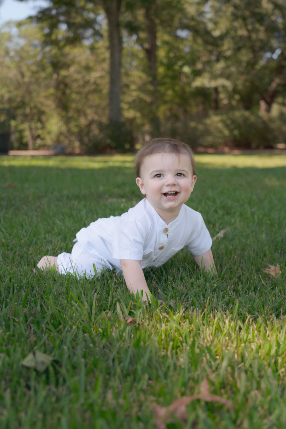 Happy baby in white outfit playing on lush green lawn.