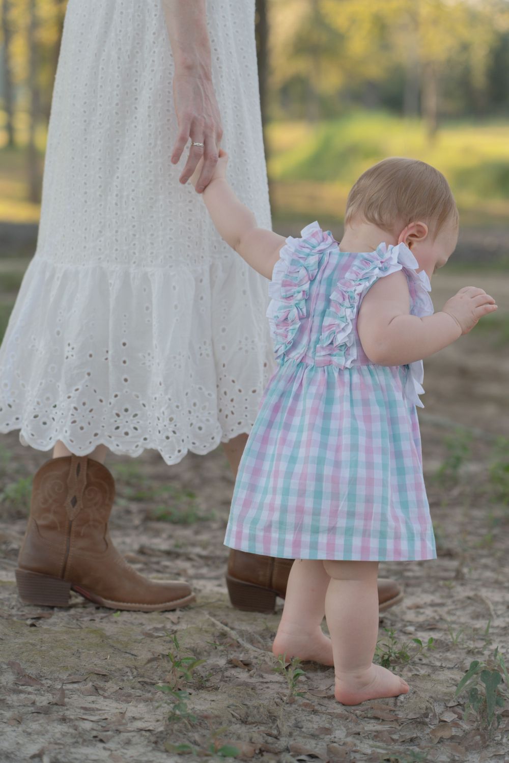 Small child in a pastel checkered dress walking barefoot next to someone in a white eyelet dress.