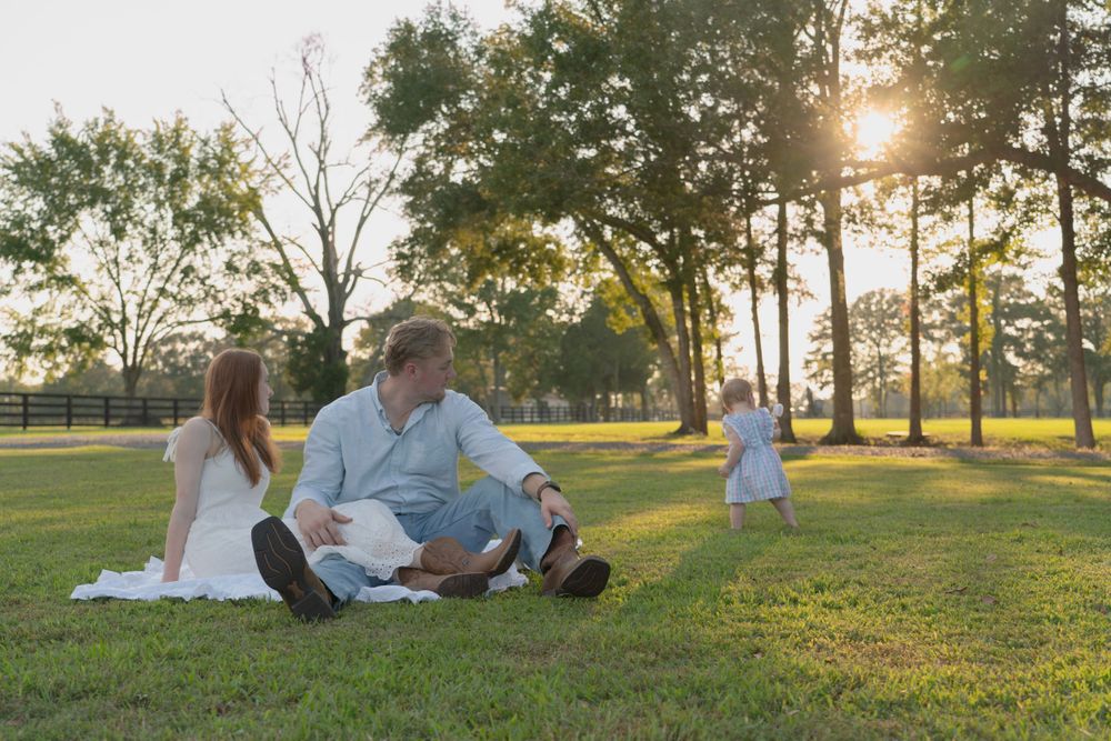 Family relaxing together on grassy hill during sunset with trees in background.