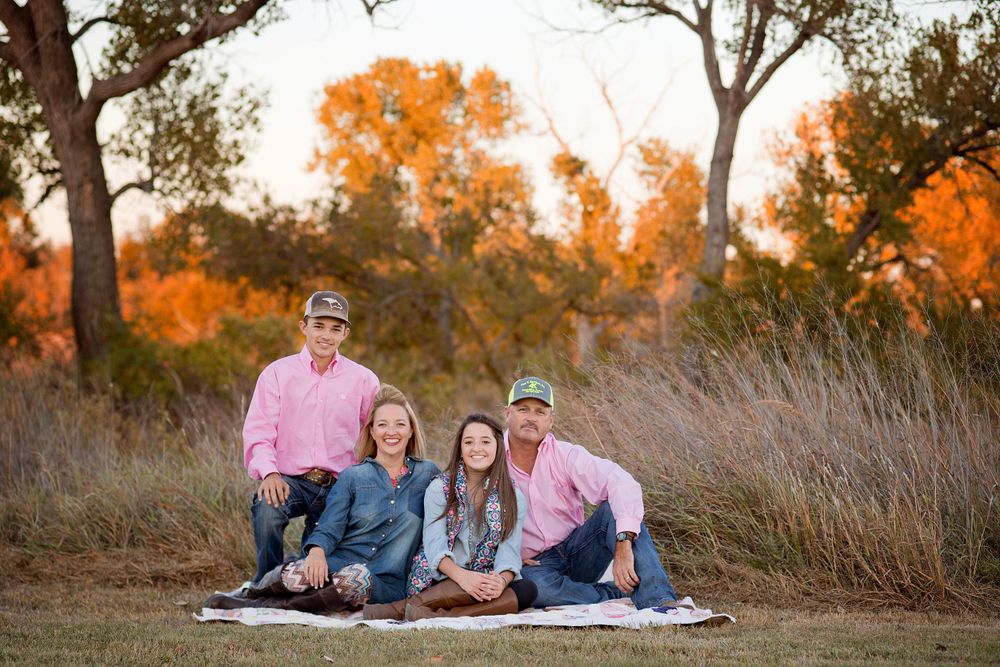 family of 4 in field sitting on quilt