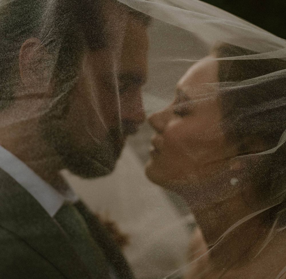Bride and groom share intimate moment under wedding veil in soft romantic close-up portrait.