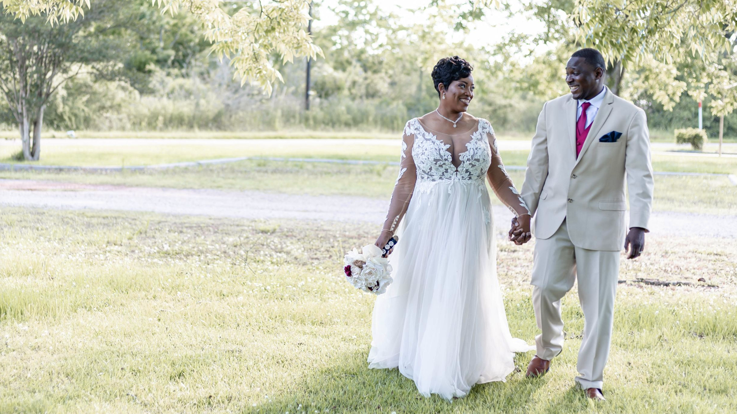 Happy couple walking through a sunny field after their wedding ceremony.