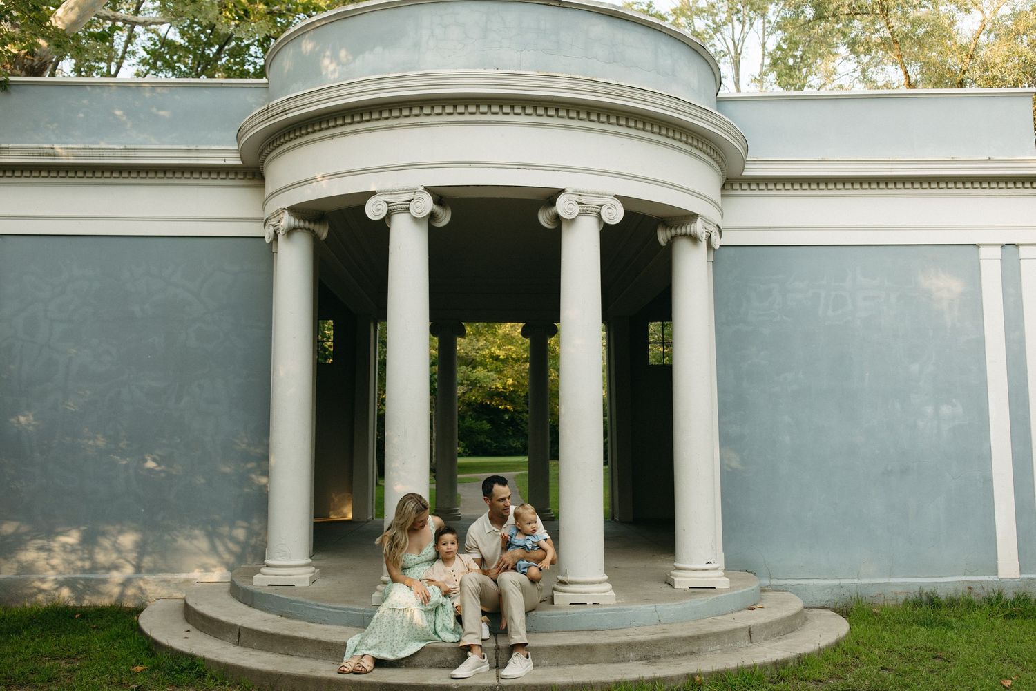 Family of four sitting on steps of a building during a golden hour session at a park