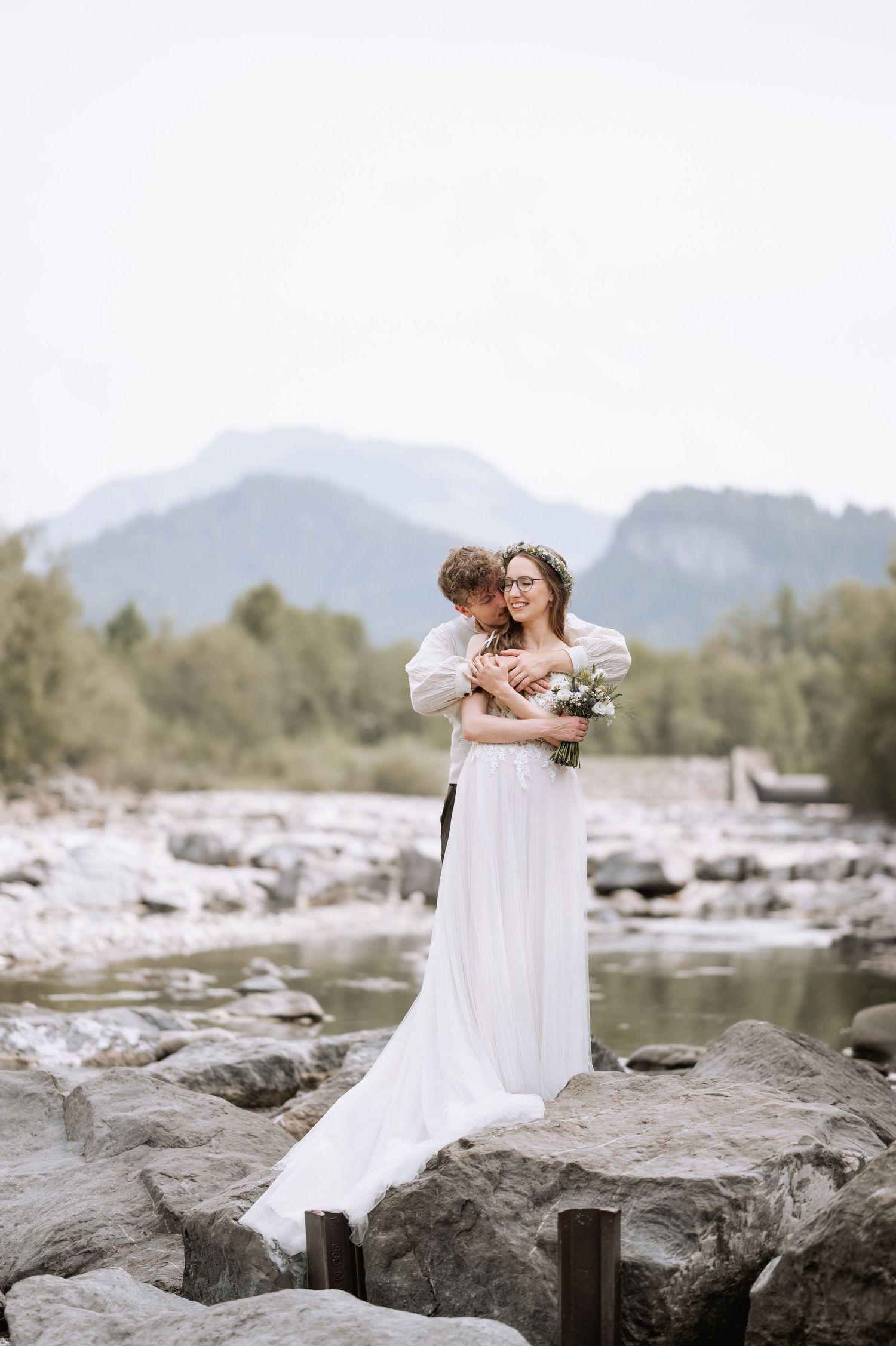 Hochzeitsshooting mit Brautpaar vor einer Bergenkulisse, während er sie hält und am Nacken küsst Jovanna Burkard