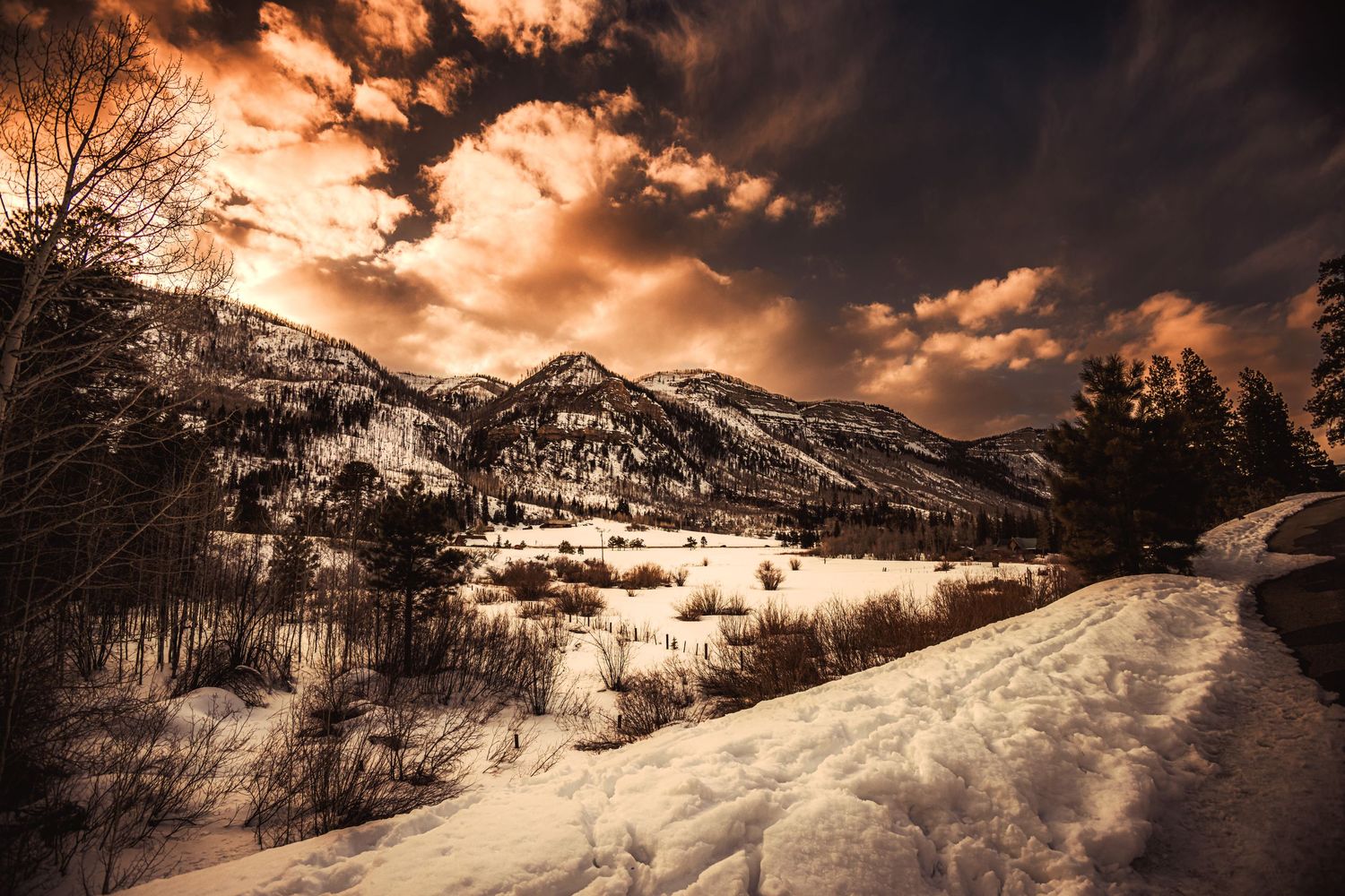 Snow covered mountain landscape with dramatic orange sunset clouds.