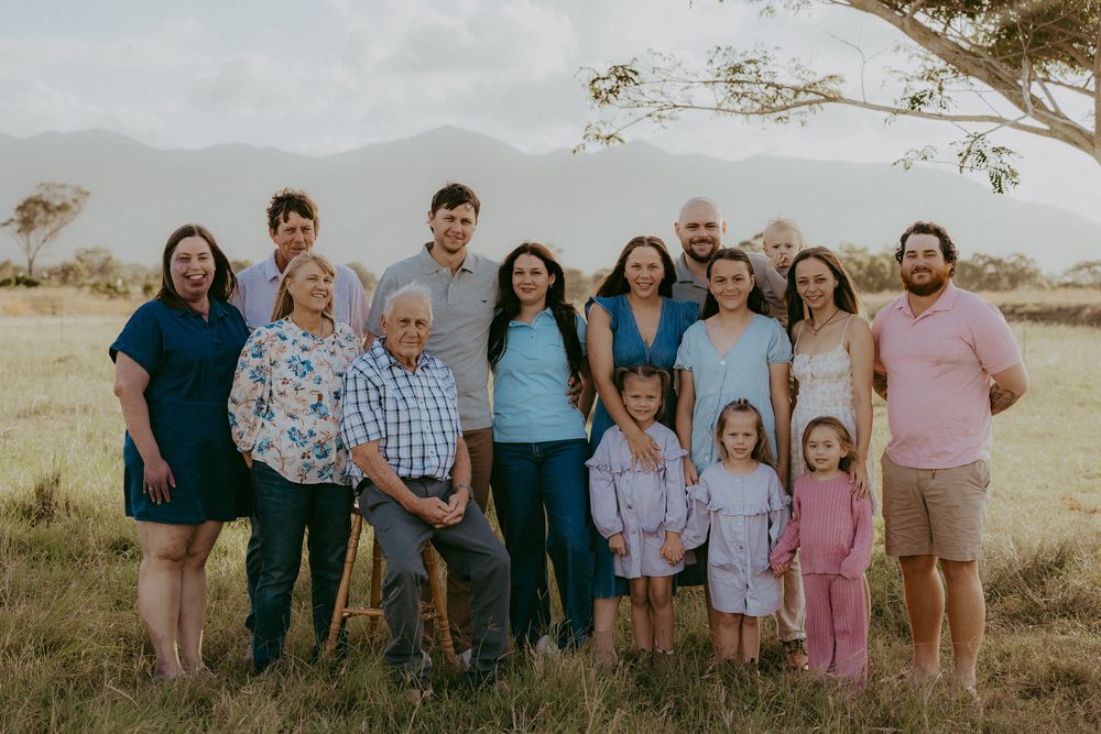 Large multigenerational family portrait outdoors in a scenic field with mountains backdrop.