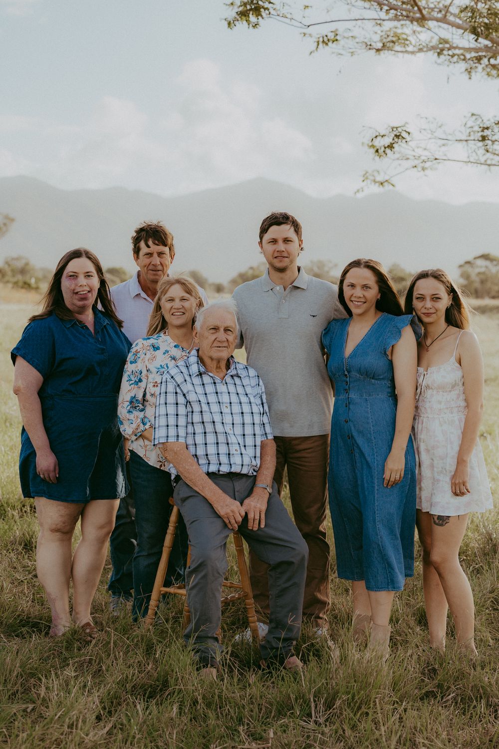 Multi-generational family of seven posing together in a grassy field with mountain views.