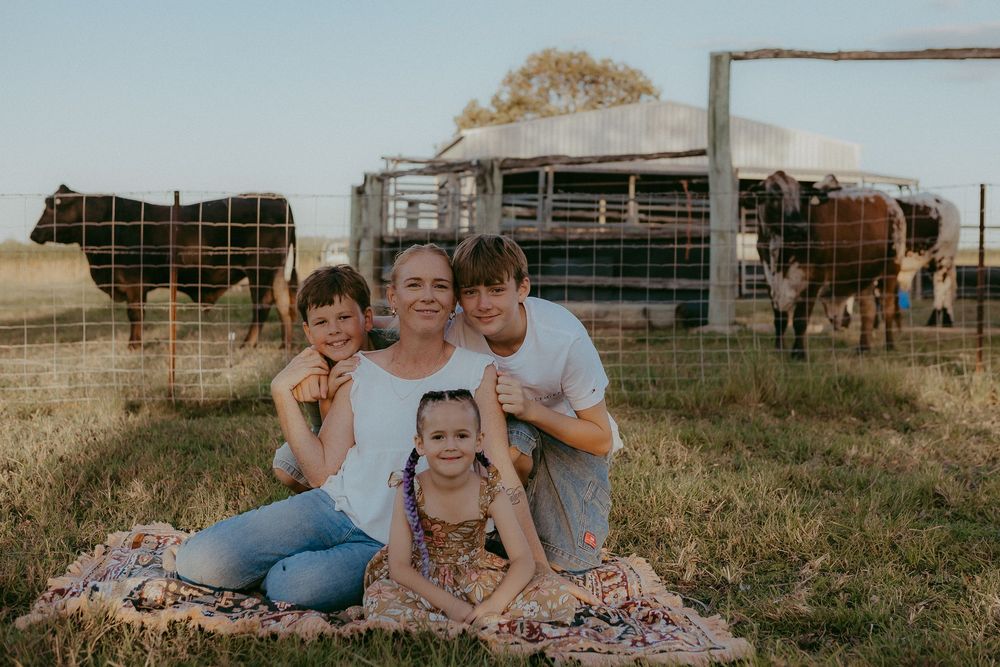 Mother with three children sitting on blanket in field with cattle grazing behind them.
