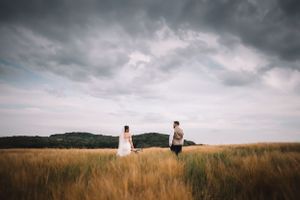 A wedding couple stand in a golden wheat field beneath dramatic stormy clouds in a moody landscape scene at Swancar Farm, Nottingham.