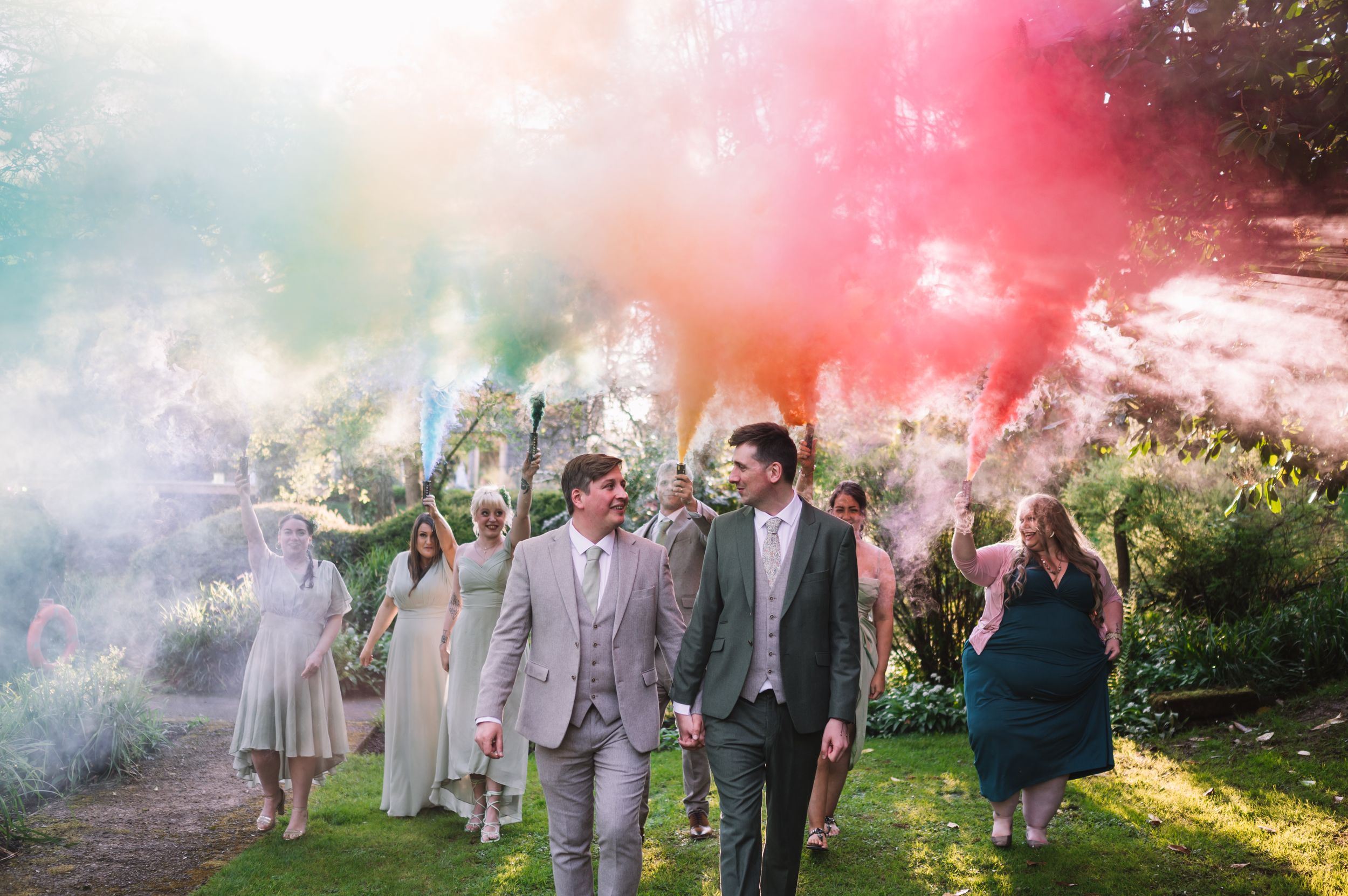 Wedding party celebrates with colorful smoke bombs in an outdoor garden setting creating vibrant atmosphere at the Mill Barns.