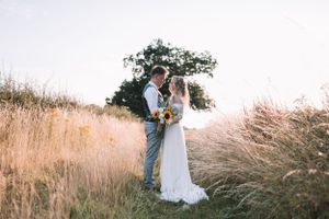 A couple stand together in a golden wheat field at sunset, surrounded by tall wild grass at Hanbury Barns, Staffordshire.
