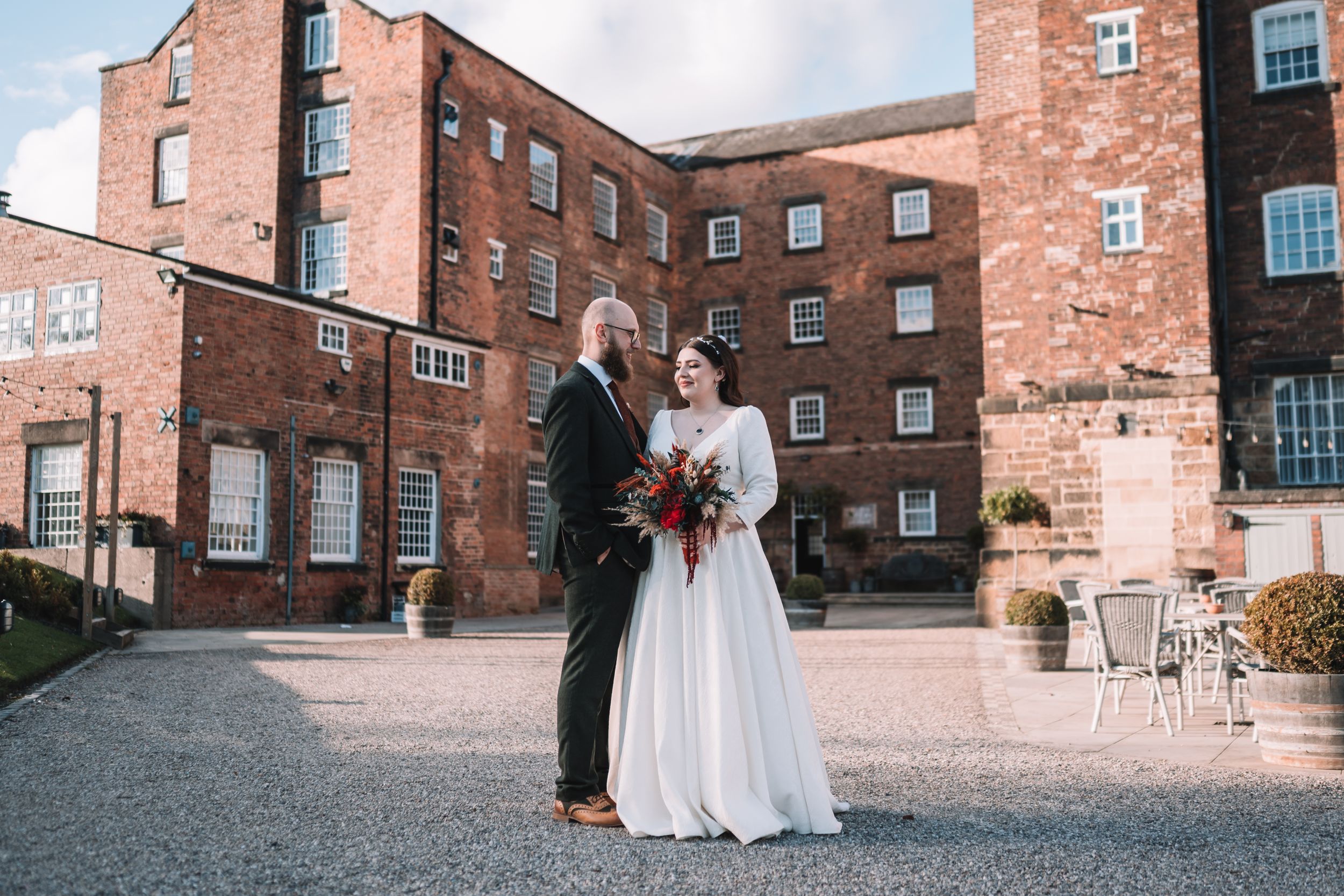 A couple shares an intimate moment in front of a rustic brick building on their wedding day at the West Mill, Darley Abby, Derby.