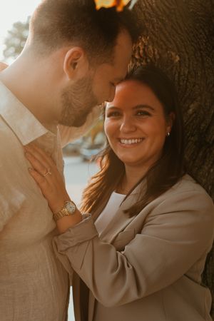 Intimate engagement photos captured in warm sunlight against a tree.