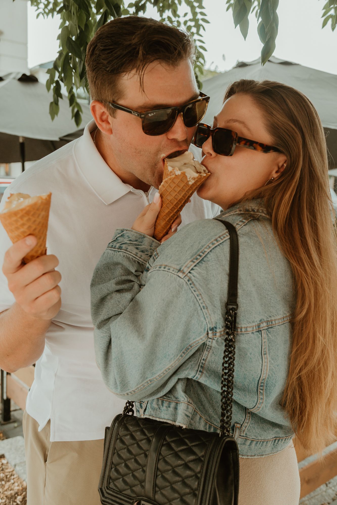 Playful couple sharing ice cream cones while wearing matching sunglasses and casual attire.