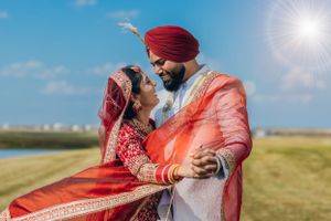Romantic moment captured between couple in traditional Sikh wedding attire outdoors in golden sunlight.