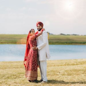 Wedding couple in traditional Sikh attire embracing by lakeside in natural setting.
