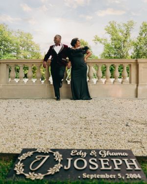 A couple in formal black attire walks on a terrace with their wedding date displayed in the foreground.
